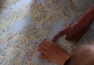 Joseph Ottawa, aîné atikamekw nehirowisiw  de 81 ans ayant participé au projet matakan depuis  le début, montre aux jeunes sur une carte, différents endroits du Nitaskinan avec les histoires qui y sont associé.
Photo : Étienne Levac, 2020